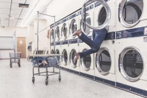 Photo of a person's legs dangling out of a machine in a laundromat. Photo courtesy of Ryan McGuire from Pixabay.